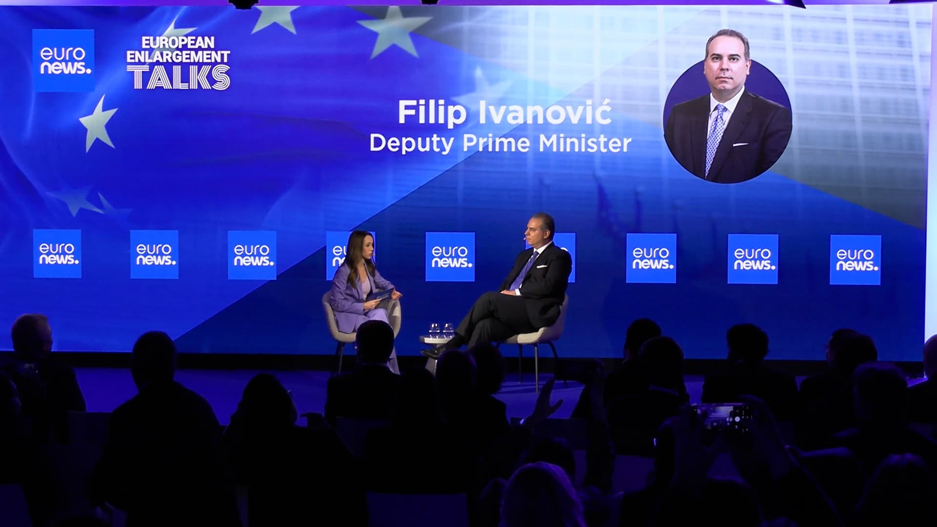 A host in conversation with a guest on a European stage